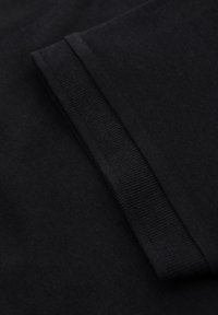 Černá bavlněná látka s hladkým povrchem; má žebrovaný manžet a pečlivé švy podél okrajů. Jednoduchý, minimalistický design.