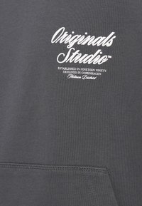 Šedá mikina s přední kapsou, žebrovanými manžetami a bílým logem s nápisem "Originals Studio" a údaji o založení pod ním.