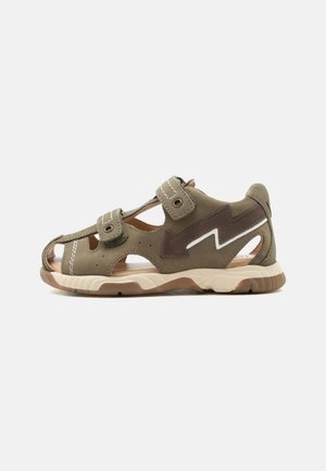 Κλειστή παιδική σάνταλ σε ελιά πράσινο χρώμα με δύο ρυθμιζόμενα λουριά βέλκρο και καφέ σχέδιο κεραυνού στο πλάι.