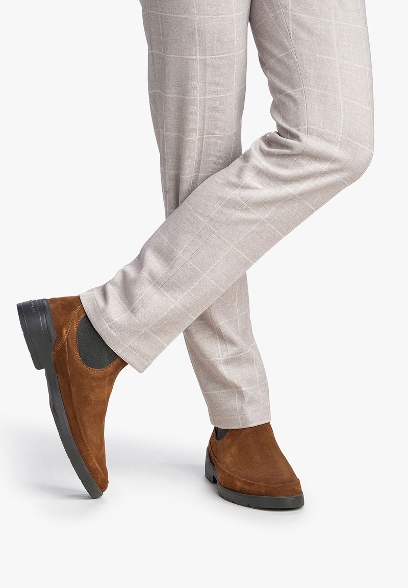 Bottines en suédine marron avec des inserts élastiques sur les côtés, associées à un pantalon à carreaux gris clair. Le pantalon a une coupe slim et une texture lisse.