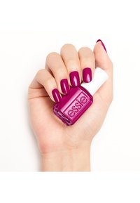Vernis à ongles fuchsia vif dans un flacon en verre avec un bouchon blanc, tenu par une main aux ongles manucurés de la même couleur.