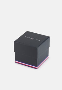 Schwarze rechteckige Geschenkbox mit einem Deckel, der oben ein Logo und entlang der unteren Kante einen farbigen Streifen (rot, weiß, blau) aufweist.