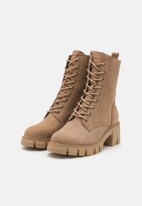 Botas de tobillo de ante marrón con cordones en la parte delantera, puntera redonda, tacones gruesos y costuras reforzadas para una mayor durabilidad. Superficie texturizada.