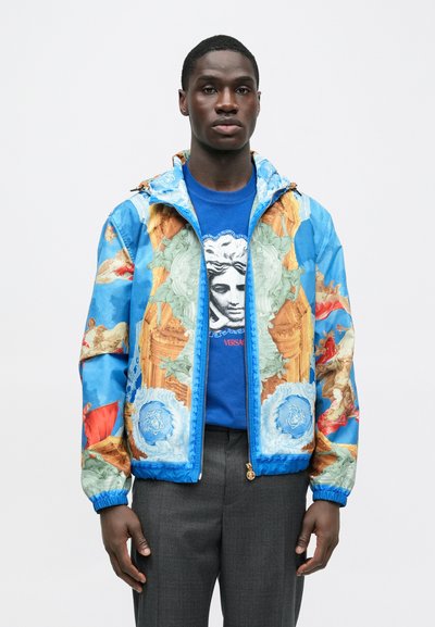 Barvita srajca z vzorcem v modrih in oranžnih tonih, ki upodablja klasične umetniške elemente, z elastičnimi manšetami in zadrgo spredaj.