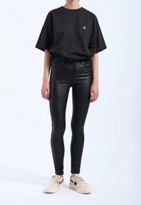 Czarny, oversize'owy t-shirt, czarne obcisłe jeansy z połyskującym wykończeniem oraz kremowe sneakersy z czarnymi akcentami. Bez wyraźnych wzorów czy grafik.