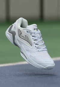 Bílé sportovní boty s prodyšným svrškem, hladkými syntetickými akcenty a polstrovanou podešví. Logo a název modelu viditelné na jazyku.