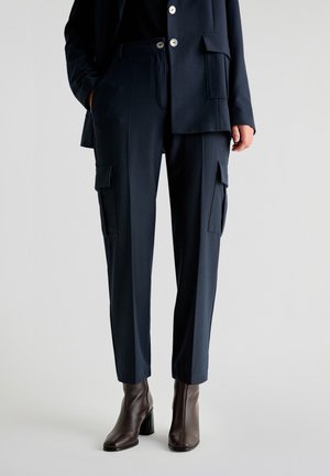 Pantaloni cargo blu impostati con tessuto testurizzato, dotati di due tasche laterali e un design a gamba dritta. Indossati con stivaletti con tacco marroni.
