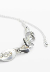 Collar de cadena plateada con eslabones grandes de formas ovaladas abstractas y en forma de gota, conectados por cadenas más pequeñas sobre un fondo blanco.