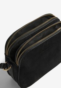 Borsa rettangolare nera in suede con due zip dorate e una tracolla in pelle nera attaccata da un anello dorato.