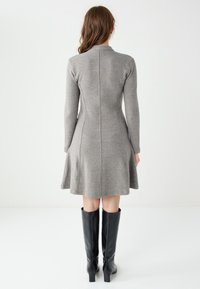 Grijze gebreide jurk met lange mouwen en een uitlopende zoom, met een naaddetail in het midden op de rug. Gecombineerd met hoge zwarte laarzen.
