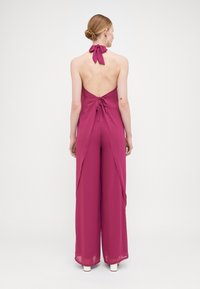 Combinaison halter fuchsia avec un dos nu, nouée au cou, dotée de jambes larges et amples et d'un tissu doux et fluide.