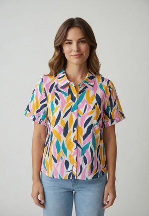 Giovane donna con capelli castani ondulati indossa una camicia a maniche corte con bottoni, decorata con motivi astratti colorati a forma di foglia, e jeans azzurri.