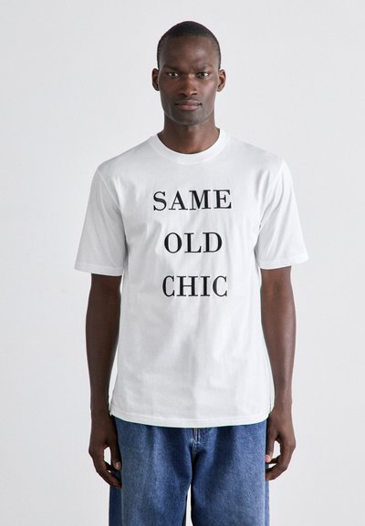 T-shirt en coton blanc avec un texte noir en lettres majuscules "SAME OLD CHIC" centré sur le devant. Manches courtes et encolure ronde. Coupe décontractée.