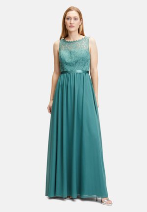 Türkises Abendkleid mit einem Spitzenoberteil, ärmellosem Design und einem fließenden Rock mit einem Satinbund. Silberne Absätze ergänzen das Outfit.