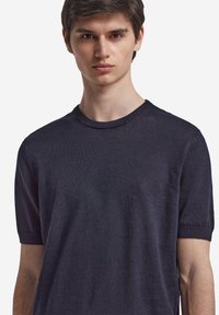 Marinblå t-shirt med rund hals i lätt material, kort ärm och ribbad krage, med en mjuk textur och minimalistisk design.