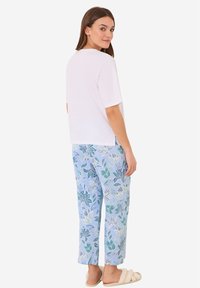 Witte top met korte mouwen en ronde hals, gecombineerd met lichtblauwe broek met een bloemenpatroon in groen en teal; zachte stoftextuur.