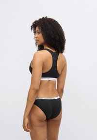 Μαύρο αθλητικό σουτιέν με σχέδιο racerback και λευκή ταινία με λογότυπο. Τα εσώρουχα ταιριάζουν, με παρόμοια ταινία με λογότυπο. Ομαλή υφή υφάσματος.