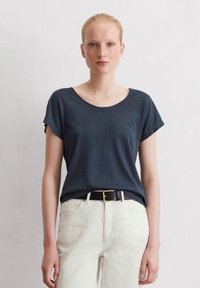 Granatowy t-shirt z krótkim rękawem o okrągłym dekolcie, wykonany z miękkiego materiału, zestawiony z jasnymi spodniami i czarnym paskiem.