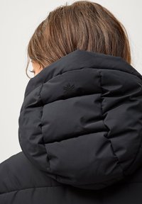Zwarte gewatteerde jas met een hoge kraag, voorzien van een soepele textuur en een klein zwart logo op de achterkant van de kraag.