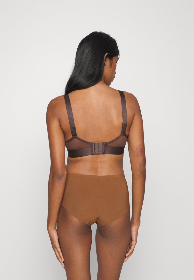 Sosten en color marrón con detalles de malla y tirantes ajustables, con un cierre de gancho y ojal en la parte posterior. Combinado con panties marrones de tiro alto y sin costuras.