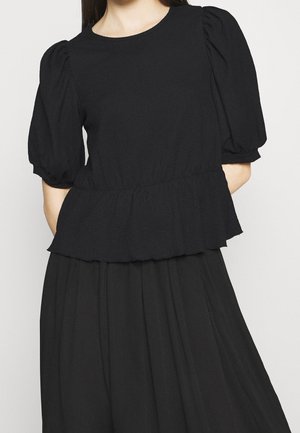 Blusa nera con maniche a sbuffo, finitura testurizzata e vita a pipistrello. Il collo è rotondo senza ulteriori decorazioni.