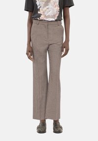 Beżowe spodnie w kratkę z wysokim stanem i szerokimi nogawkami. Materiał wydaje się teksturowany, w połączeniu z czarnym t-shirtem z grafiką i szarymi mokasynami.