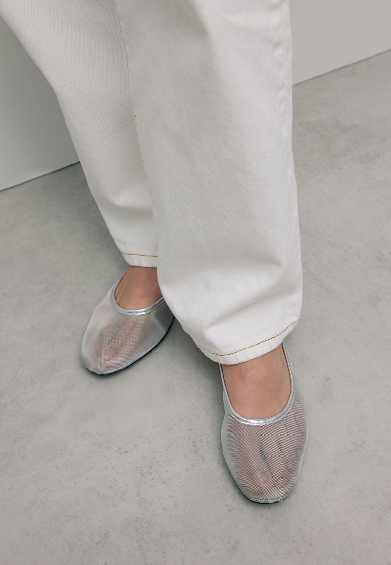 Transparante mesh instap schoenen met een ronde neus, zilveren accenten en een flexibele zool, gecombineerd met witte broekspijpen tot de enkel.