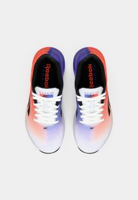 Reebok Nano X1 kedas ar ombre dizainu, kas pāriet no sarkanas uz purpura krāsu, ar melnu iekšpusi un baltām šņorēm. Melni akcenti sānos.