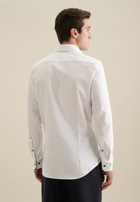 Witte lange mouwen shirt met een klassieke kraag, zachte stof en zwarte knoopaccenten op de manchetten en de rug. Tapered fit.