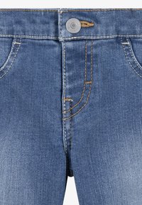 Jeans iz denima v srednji modri barvi, z zadrgo in gumbom, ter kontrastnim zlatim šivom. Ima štiri žepe z diskretnim zbledeljem.