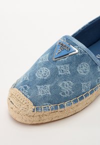 Blauwe denim espadrille met een geperst patroon, jute zool en een driehoekig metallic logo-accent. Rond neusdesign en gestikte details.