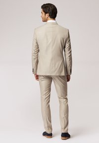 Hellbeige Anzug mit taillierter Passform, Ein-Knopf-Blazer und flach geschnittenen Hosen. Glatte Textur, dezentes Muster und schwarze Schuhe.