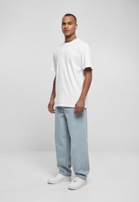 White cotton t-shirt with short sleeves, paired with light blue denim relaxed-fit pants and white sneakers. Minimalistic design.