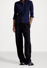 Námornická polokošile s dlouhým rukávem, knoflíky a červeným logem, doplněná širokými černými kalhotami a barevnými sportovními botami.