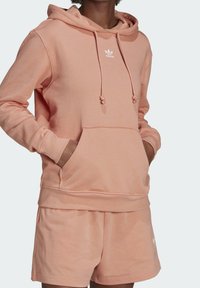 Rosa bomullshuvtröja med dragsko, kenguruficka, ribbade muddar och nederkant. Har en vit logotyp på bröstet. Kombinerad med matchande shorts.