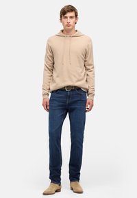 Beżowa bluza z kapturem, niebieskie jeansy o prostych nogawkach oraz beżowe zamszowe botki. Gładka faktura, sznurki przy kapturze i standardowy krój.