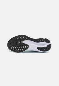 Semelle de chaussure de sport noir et blanc avec un design en caoutchouc texturé, présentant des rainures et une section médiane blanche lisse et incurvée.