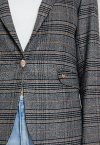 Vävd rutigt kavaj i grått, svart och brunt med en enkel knapplåsning och en framficka, med en strukturerad tyg och klassiska slag.