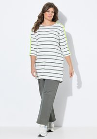 Gestreepte tuniek in wit en donkergroen met driekwartmouwen en neon gele accenten. Gepaard met grijze wijde broek en sneakers.