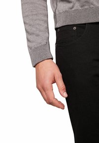 Szary sweter dziany z ściągaczami noszony na czarnych dżinsach o gładkiej fakturze i widocznym okuciu na przednich kieszeniach.