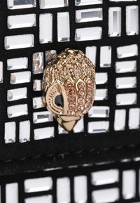 Material nero con una griglia di ornamentazioni rettangolari trasparenti. Presenta un accento dorato con motivi decorativi e cristalli.