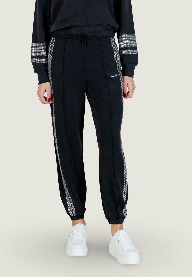 Black sweatpants with silver stripe accents, drawstring waist, and tapered cuffs, paired with white platform sneakers.