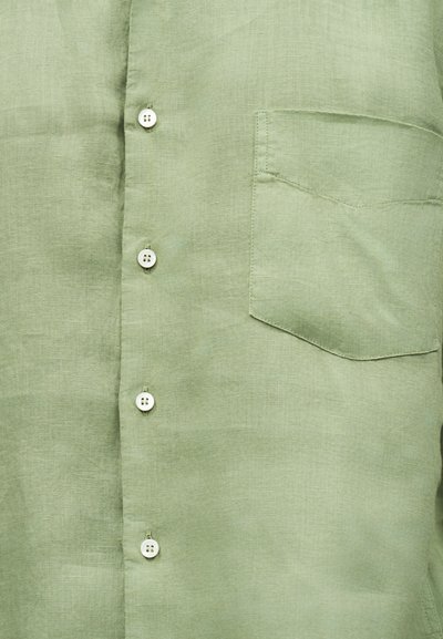 Φωτεινό πράσινο λινό πουκάμισο με λευκά κουμπιά κλεισμένα και τσεπάκι στο στήθος ραμμένο στη δεξιά πλευρά.