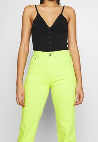 Zwarte geribbelde bodysuit met een diepe V-hals en details met vetersluiting, gecombineerd met hoog taak neongele wijde jeans.