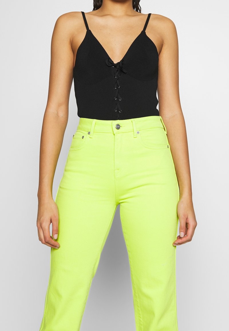 Zwarte geribbelde bodysuit met een diepe V-hals en details met vetersluiting, gecombineerd met hoog taak neongele wijde jeans.