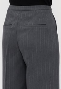 Grijze pinstriped op maat gemaakte trousers met achterkant paspelzakken en een hoge tailleband, gedragen met een zwart topje erin gestoken.