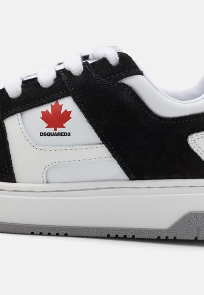 Zapatillas de gamuza negra y piel blanca con una suela gris. Presentan un logo de hoja de arce roja y la marca DSQUARED2 en el costado.