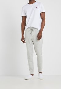 Valkoinen puuvillainen t-paita, jossa pieni punainen logo, yhdistetty vaaleanharmaisiin fleece-jogginghousuihin, joissa on joustava vyötärönauha ja kiristysnyöri. Valkoiset lenkkarit.