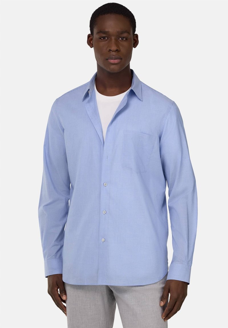 Camicia azzurra chiara a maniche lunghe con righe bianche verticali, chiusura a bottoni sul davanti, taschino sul petto e colletto aperto. Tessuto misto cotone.