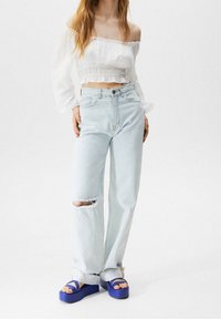 Lyseblå højtaljede jeans med et distressed knæ, parret med en hvid off-the-shoulder crop top og blå platform sandaler.